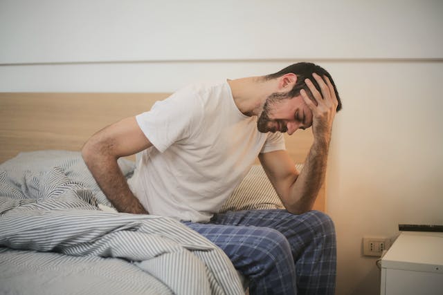 person sitting in bed holding their head in pain from headache